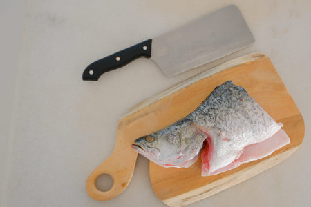 Fresh snapper fish on a wooden cutting board in a kitchen with a knife nearby
