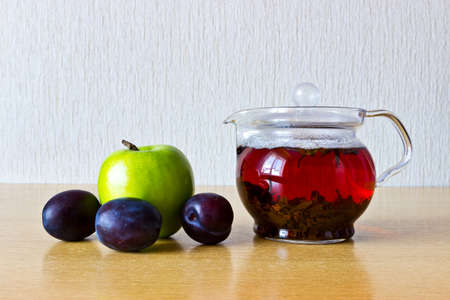 Strong black ceylon tea in glass teapot with fresh fruits: apple and prunesの写真素材