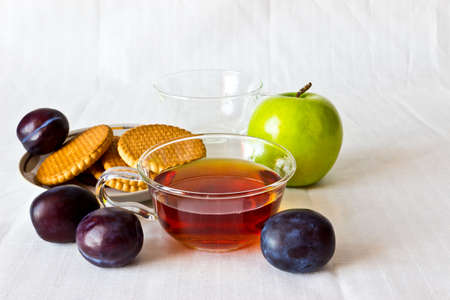 Strong black ceylon tea with cookies and fresh fruits: apple and prunes. White backgroundの写真素材