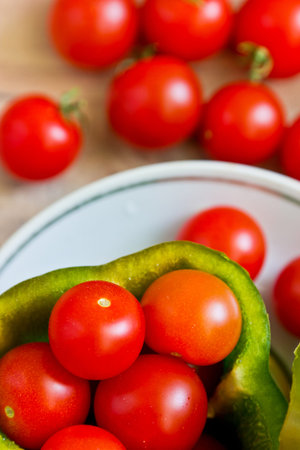 Small tomatoes in cut green pepper on white dish close up at wooden background. Vertical image with...