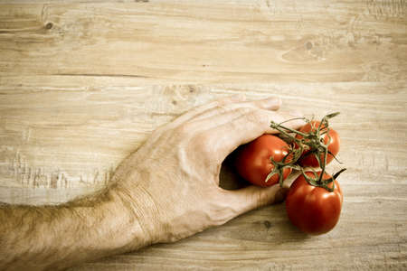 Hand takes fresh tomato from wooden table. Horizontal image with vintage filterの写真素材