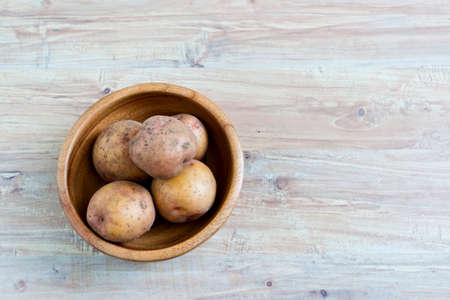 Fresh harvested potato in wooden bowl at wooden background. Horizontal image. Object in the left part of imageの写真素材