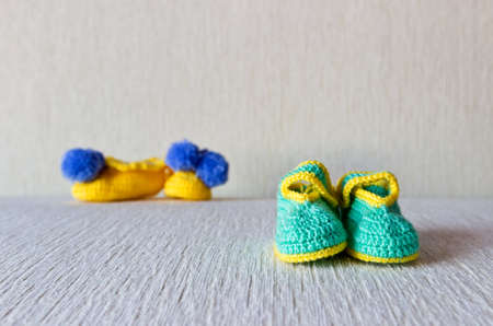 Homemade knitted small baby wool shoes. Two couple. Selective focus on green bootiesの写真素材