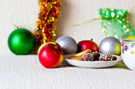 Christmas composition close up: morning tea with cookies and candies, apples, silver and green christmas balls, gift with colorful backgroundの写真素材