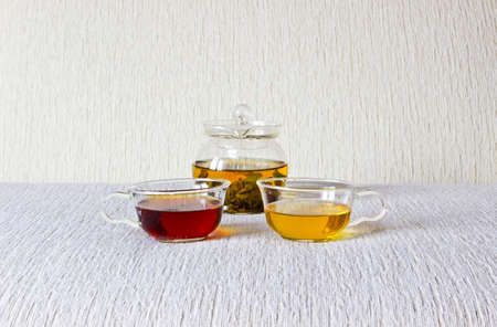 Green tea and strong black tea with fresh mint in glass cups and teapot on textured linen backgroundの写真素材