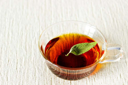 Fresh strong black tea with mint leaf in glass cup on textured linen backgroundの写真素材
