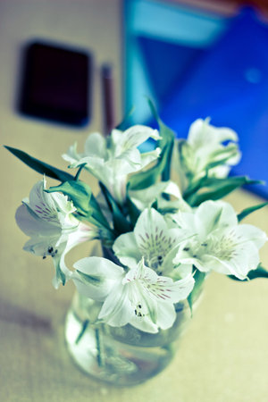 Office composition: bouquet of white freesia flowers and smartphone. Vintage image. Focus on flowers