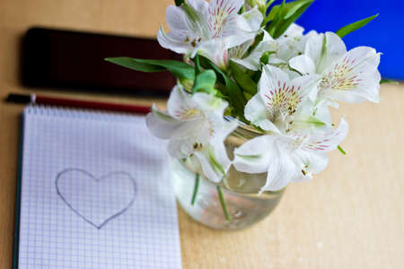 Office composition for St. Valentines Day: bouquet of white freesia flowers, smartphone, pen and notebook with painted heart. Selective focusの写真素材
