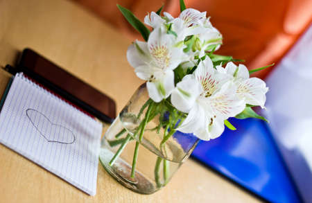 Celebrating composition: bouquet of white freesia flowers, smartphone, pen and notebook with painted heart. Selective focus. Image with multicolored bokeh backgroundの写真素材
