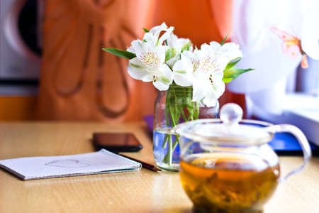 Celebrating composition: bouquet of white freesia flowers, smartphone, pen, teapot and notebook with painted heart. Selective focus. Image with multicolored bokeh backgroundの写真素材