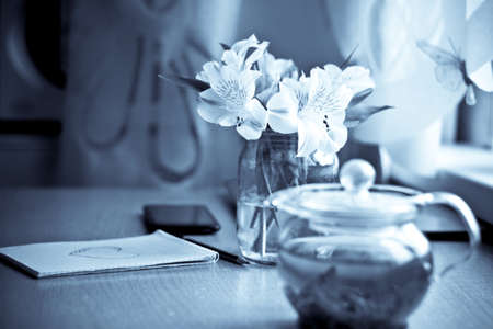Spring composition for St. Valentines Day: bouquet of white freesia flowers, smartphone, pen and notebook with painted heart. Selective focus. Blurred multicolored background. Vintage imageの写真素材