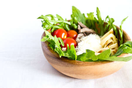 Salad of beef tongue, lettuce, tomatoes, cheese, scrambled eggs with cream and garlic sauce in wooden bowl. Selective focus. On white linen backgroundの写真素材