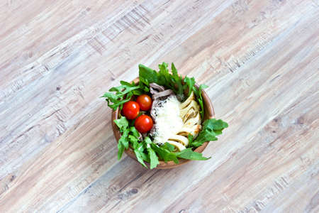 Salad of beef tongue, lettuce, tomatoes, cheese, scrambled eggs with cream and garlic sauce in wooden bowl on wooden backgroundの写真素材