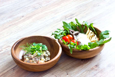 Two kinds of salads in wooden bowls: with vegetables and with beef tongue. Selective focus on wooden backgroundの写真素材