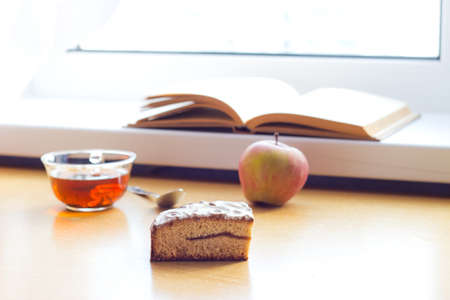 Still life composition: book tea apple cake. With selective focus and blurred background. Sunlight from windowの写真素材