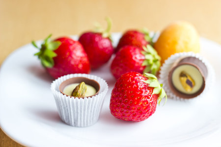 Fresh ripe strawberries, apricot and chocolate candy on white dish on wooden table