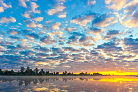 Beautiful summer sunrise with fog over the river and cloudy skyの写真素材