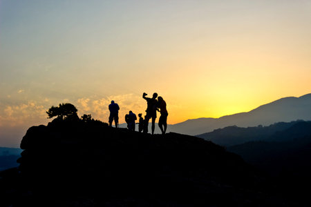 Silhouettes of people making selfie on top of rock against golden sunset