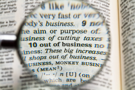 the phrase out of business in dictionary magnified by handheld magnifying glass
