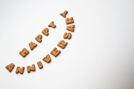 the words happy anniversary by brown biscuits on white surface in smiling arrangementの写真素材
