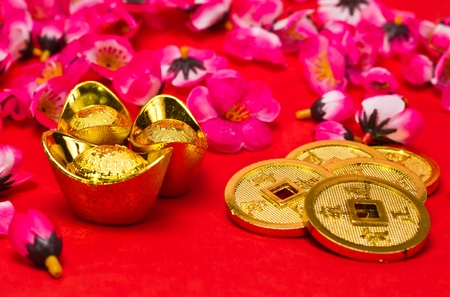 Angled view of Golden nuggets and emperors coins with cherry plum blossoms on red surface for Chinese New Yearの写真素材