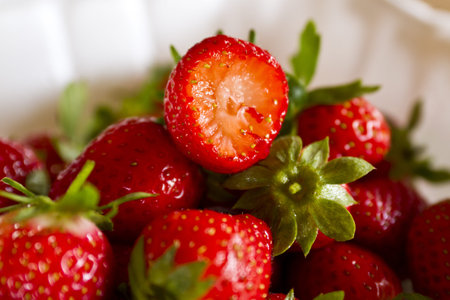 bunch of strawberries on white plastic plate with natural lighting with one bitten strawberry