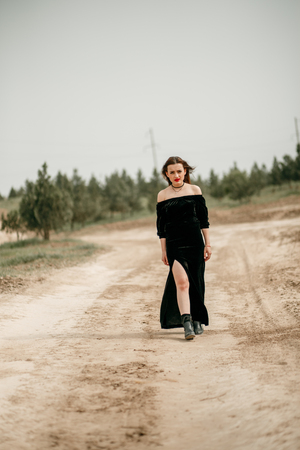 Young beautiful woman in black dress posing for a photographer on a sandy road.の写真素材