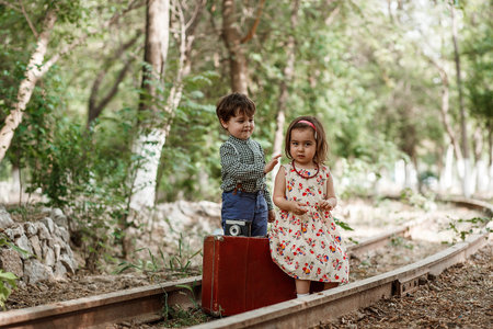 little boy and girl in vintage clothes with vintage suitcase and with vintage camera on abandoned...