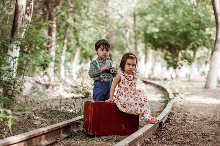 little boy and girl in vintage clothes with vintage suitcase and with vintage camera on abandoned railwayの写真素材