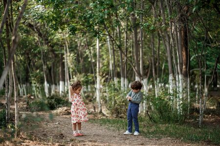 little Caucasian boy and girl in vintage clothes walking in the woods and the boy takes pictures of the girl on a retro camera. friendship and love of young childrenの写真素材