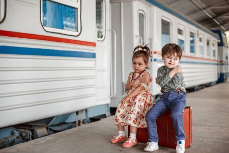 little boy and girl in vintage clothes with vintage suitcase at small railway stationの写真素材