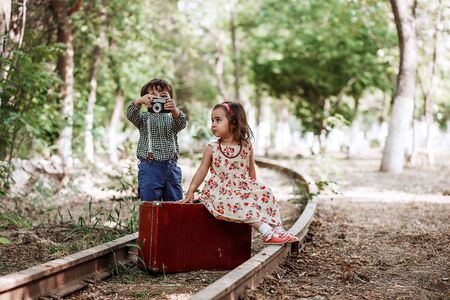 little boy and girl in vintage clothes with vintage suitcase and with vintage camera on abandoned railwayの写真素材