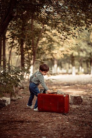 little cute boy in vintage clothes in the Park with vintage suitcase with vintage camera in handの写真素材