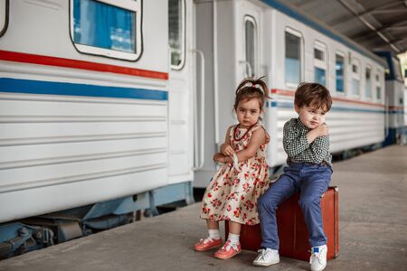 little boy and girl in vintage clothes with vintage suitcase at small railway stationの写真素材