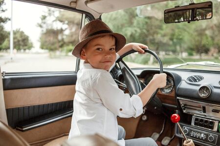 Caucasian little boy in vintage clothes sitting inside a retro carの写真素材