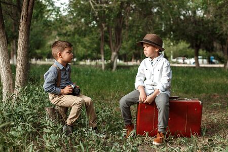 two Caucasian boy brothers in vintage clothes sit opposite each other and watchの写真素材