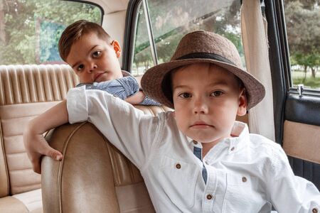 two Caucasian little boys in vintage clothes sitting inside a retro carの写真素材