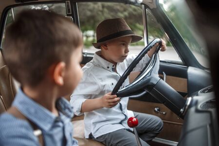 two Caucasian little boys in vintage clothes sitting inside a retro carの写真素材