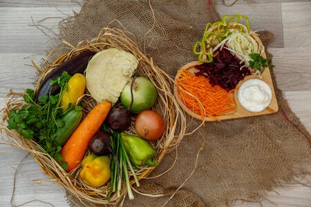 fresh vegetables,onions,cabbage,peppers,carrots ,beets in a wooden wicker basket and grated vegetables on a wooden tray in the shape of a heart with sauceの写真素材