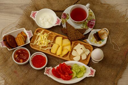 hearty and healthy Breakfast. tea in a Cup,different types of cheese on a wooden stand,sauces,boiled eggs,red caviar,cucumbers,tomatoes and jam.の写真素材
