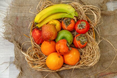 fresh fruit, apples , bananas, oranges and persimmons in a wooden basket on straw . the view from the topの写真素材