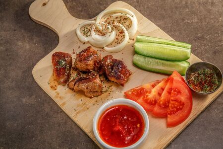 grilled meat with fresh tomatoes, cucumbers and onions with tomato hot sauce on a wooden tray.の写真素材