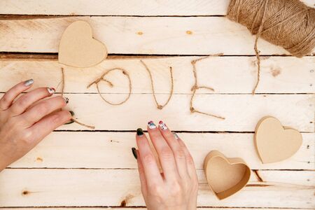 women's hands spread hearts and the word love of threads on a light wooden background. the view from the topの写真素材