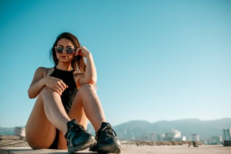 young brunette girl in black sneakers,black shorts and a black short top sitting on the roof of a tall buildingの写真素材