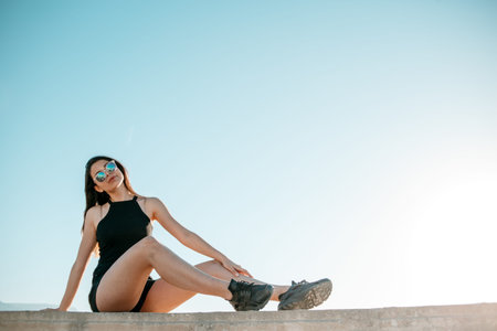 young brunette girl in black sneakers,black shorts and a black short top sitting on the roof of a...