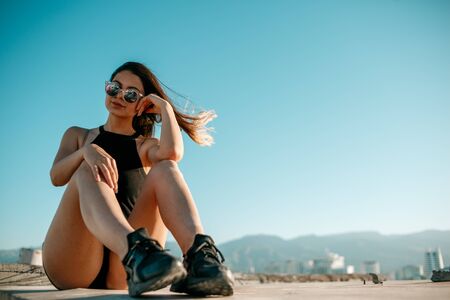 young brunette girl in black sneakers,black shorts and a black short top sitting on the roof of a tall buildingの写真素材