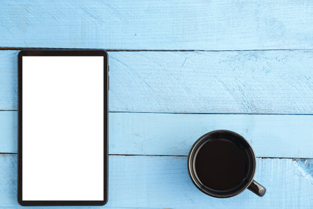 black tablet and a Cup of drink on a blue wooden background. the view from the top