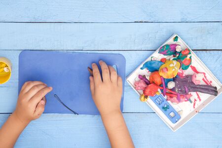 children's hands sculpt figures of clay on a blue table. the view from the topの写真素材