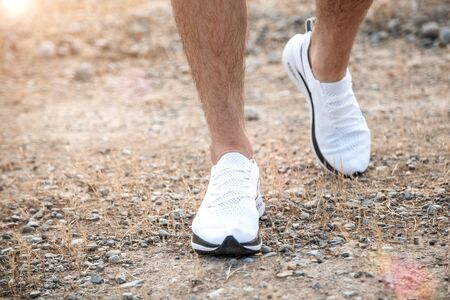 men's feet in white sneakers running over rough terrain. Cross country running with focus on runner's legs.の写真素材