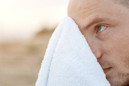 Portrait of a sporty young Caucasian guy in a black t-shirt wipes his face with a towelの写真素材